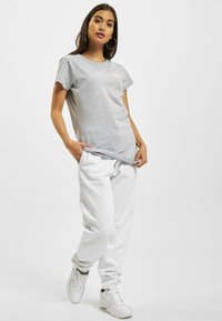 Tricou din bumbac gri cu guler rotund și mâneci scurte, asociat cu pantaloni de trening albi și adidași albi. Design simplu, stil casual.