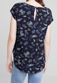 Blusa navy de manga corta, con un estampado de paisley y flores. Abertura en forma de llave en la parte posterior. Tejido ligero con un corte relajado.