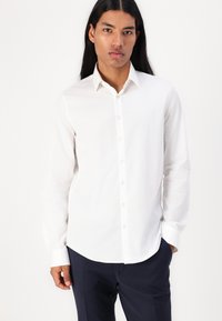 Camisa blanca de manga larga abotonada, hecha de tejido ligero, con cuello apuntado, dobladillo recto y puños de un botón.