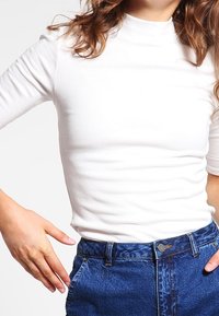 Top bianco a collo alto con righe, maniche corte, abbinato a jeans in denim blu a vita alta con passanti per cintura e chiusura a bottone.