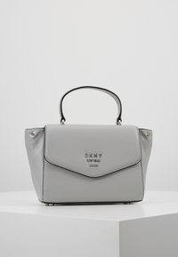 Szara torebka ze skóry o wyraźnie ukształtowanym kształcie, z rączką na górze, srebrnymi detalami oraz klapką z logo. Teksturowana powierzchnia.