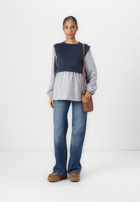 Mornarsko modra in črtasta majica z dolgimi rokavi in nabrano spodnjim delom, v kombinaciji s širokimi denim hlačami in rjavimi platform čevlji. Rjava torba preko telesa.