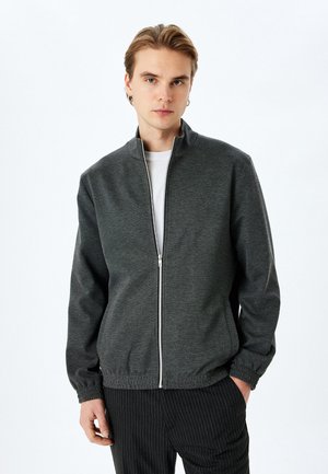 Chaqueta gris con cremallera y alto cuello, puños y cinturilla elásticos. Fabricada con un tejido texturizado; cuenta con una cremallera suave y líneas limpias.