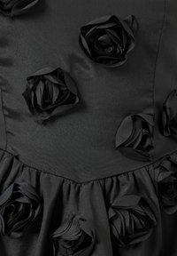 Czarna satynowa sukienka z teksturowanej tkaniny, z uniesionymi aplikacjami w kształcie czarnych róż oraz rozkloszowanym dołem z falbanką.