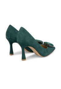 Grüne Wildleder-Pumps mit spitzem Schnitt, die vorne mit zwei großen dekorativen Kristallen verziert sind und einen schlanken Stiletto-Absatz haben.