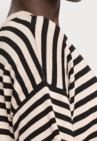 Gehaakte trui met horizontale zwarte en lichtbeige strepen. De stof lijkt zacht, met een losse pasvorm en een lichte textuur.