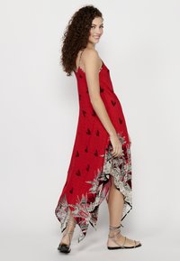 Robe rouge fluide avec un motif de feuilles noires, ourlet asymétrique et bordure en dentelle florale blanche. Fines bretelles et tissu léger.
