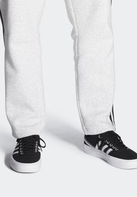 Harmaat collegehousut pehmeällä pinnalla ja mustilla raidoilla sivuilla, yhdistettynä mustiin lenkkikenkiin, joissa on valkoiset pohjat ja nauhat.