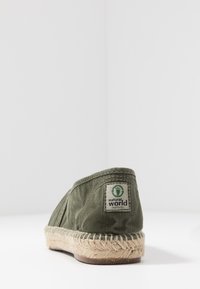 Espadrillas in tela verde con suola in fibra naturale, caratterizzate da un bordo cucito e un piccolo etichetta con il logo "natural world" sul tallone.