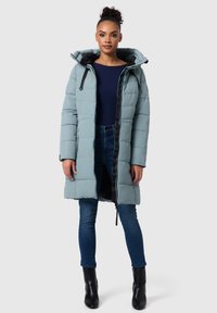 Lichtblauwe gewatteerde jas met capuchon, voorzijde met rits, zwarte accenten en een losse pasvorm, gedragen over een marineblauw topje en denim jeans.