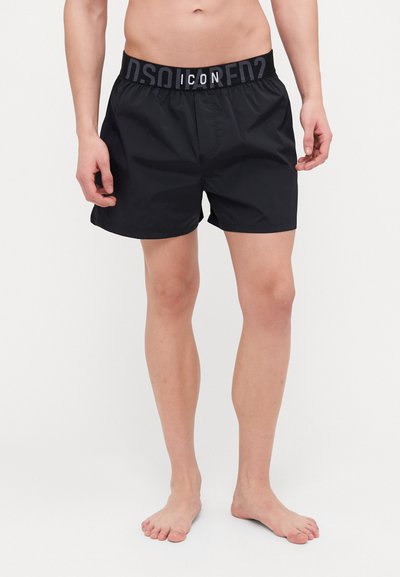 Schwarze Badeshorts aus leichtem Material, mit elastischem Bund, auf dem "ICON" gedruckt ist. Einfaches, funktionales Design.