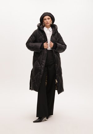 Abrigo acolchado negro con capucha, con un diseño de rombos, cierre de cremallera en la parte delantera y forro de estampado de leopardo. Combinado con pantalones negros de pierna ancha.