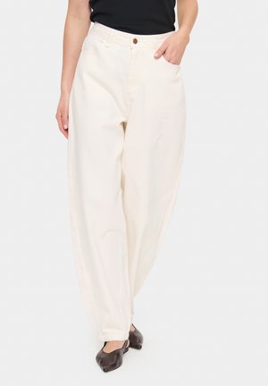 Cream-colored wide-leg trousers made of cotton, featuring a button closure and side pockets, displayed with a hand resting in one pocket.