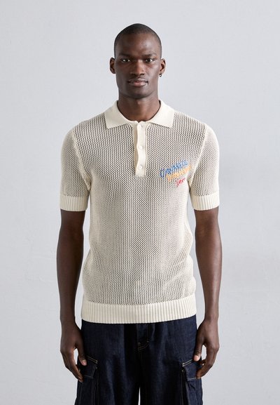 Polo shirt tricotat de culoare crem, cu mâneci scurte, având o textură din plasă, cu o deschidere cu trei nasturi și accente brodate în albastru și roșu.