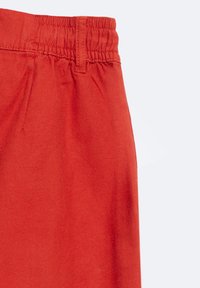 Pantalones cortos de algodón rojos con una cinturilla elástica, que presentan una textura suave y costuras limpias, parcialmente visibles en la imagen.