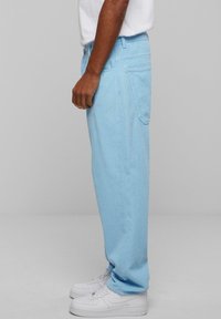 Light blue corduroy pants with a straight cut, side pockets, and visible stitching, paired with white sneakers.