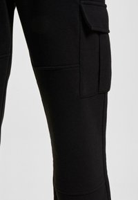 Pantaloni cargo negri dintr-un material moale, cu buzunare laterale, croială ajustată și detalii de cusătură vizibile pe cusături.