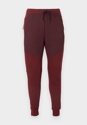 Pantaloni de sport maroon cu un design conic. Materialul este neted, având un panou roșu contrastant și buzunare laterale. Talie ajustabilă cu șnur.