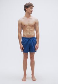 Μπλε μαγιό σορτς με ελαστική μέση και κορδόνι. Ομαλή υφή, μήκος μέχρι το γόνατο, χωρίς ορατά σχέδια ή εξαρτήματα.