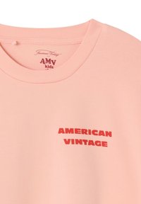 T-shirt en coton rose avec un col rond côtelé et un texte imprimé en rouge indiquant « AMERICAN VINTAGE » en caractères gras et modernes.