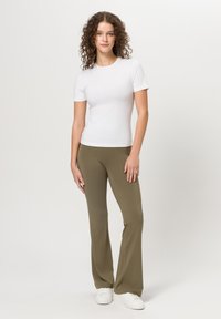Bílé přiléhavé tričko v kombinaci se zelenohnědými rozšířenými kalhotami. Lehký materiál, krátké rukávy a hladká textura. Bílé tenisky dotvářejí vzhled.