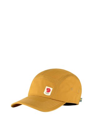 Cappellino giallo senape con visiera curva, cuciture visibili, piccolo logo a forma di volpe sul davanti e una piccola etichetta con la bandiera svedese sul lato.