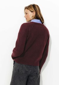 Pull bourgogne à coupe décontractée, en texture tricotée, avec des manches raglan, associé à un jean gris taille haute.