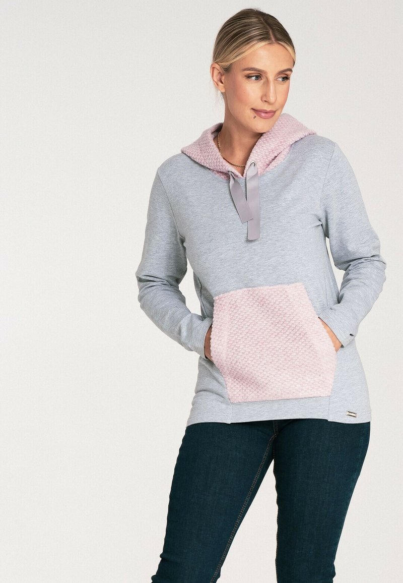 Szary hoodie z różową, teksturowaną kieszenią i kapturem. Posiada płaskie sznurki i długie rękawy. Wykonany z miękkiego materiału o luźnym kroju.