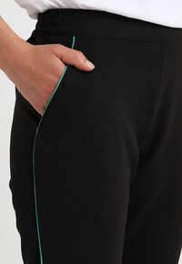 Svarta joggers i mjukt material har en avslappnad passform, ett elastiskt midjeband och kontrasterande grön kant längs sidofickan.