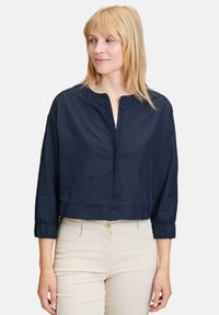 Veste courte bleu marine avec un col rond, des poignets élastiques et une texture lisse. Dotée d'une fermeture éclair à l'avant et d'un design minimaliste.