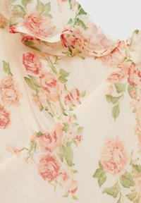 Tissu léger à motif floral avec un fond crème, présentant des roses roses et vertes, et des bords délicatement froncés.