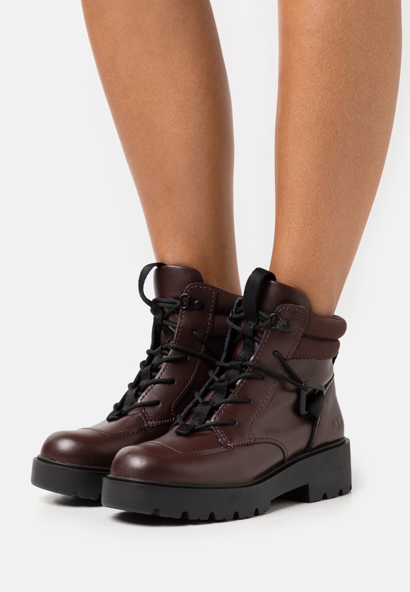 Bottines en cuir marron avec lacets noirs, semelle en caoutchouc, col rembourré et détails de couture discrets. Texturées pour le confort et la durabilité.