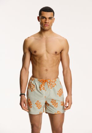 Shorts de bain vert clair avec des motifs abstraits en forme de corail orange, taille élastique et cordon de serrage, fabriqués en tissu léger.