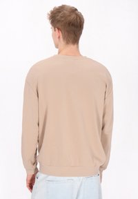 Beige sweatshirt hosszú ujjakkal, bordás mandzsettával és hemmel, kerek nyakkal és laza szabással; világoskék farmerral viselve.
