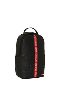 Zaino nero in materiale testurizzato, con un design di squalo prominente e una tracolla rossa incisa con "SPRAYGROUND SHARK CENTRAL NY."