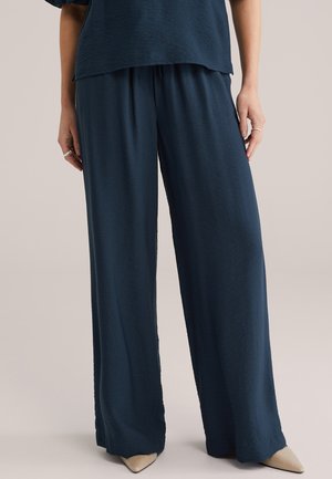 Marineblauwe wijde broek van gestructureerde stof met een elastische tailleband. Gecombineerd met puntige beige hakken voor contrast.