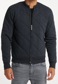 Vadderad bomberjacka i mörk marinblå, med rundad krage, dragkedja fram, ribbade muddar och midja, med en slät yta.