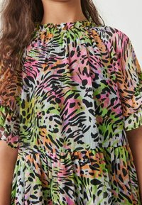 Barevné šaty s volánkovým výstřihem, které mají živý zvířecí vzor v růžové, zelené, černé a oranžové na lehké, plissé tkanině.