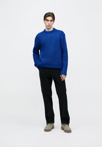 Kék kötött pulóver kerek nyakkal, fekete nadrággal és bézs csizmával párosítva. A szövet strukturált mintával rendelkezik.