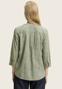 Chemise à manches longues verte à carreaux avec option de rouleau boutonné, coupe décontractée et pli au dos pour plus de liberté de mouvement, en tissu texturé.