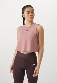 Crop top i blød lyserød stof med rund halsudskæring og detaljer med sort logo. Sæt sammen med mørkebrune leggings med et hvidt logo.