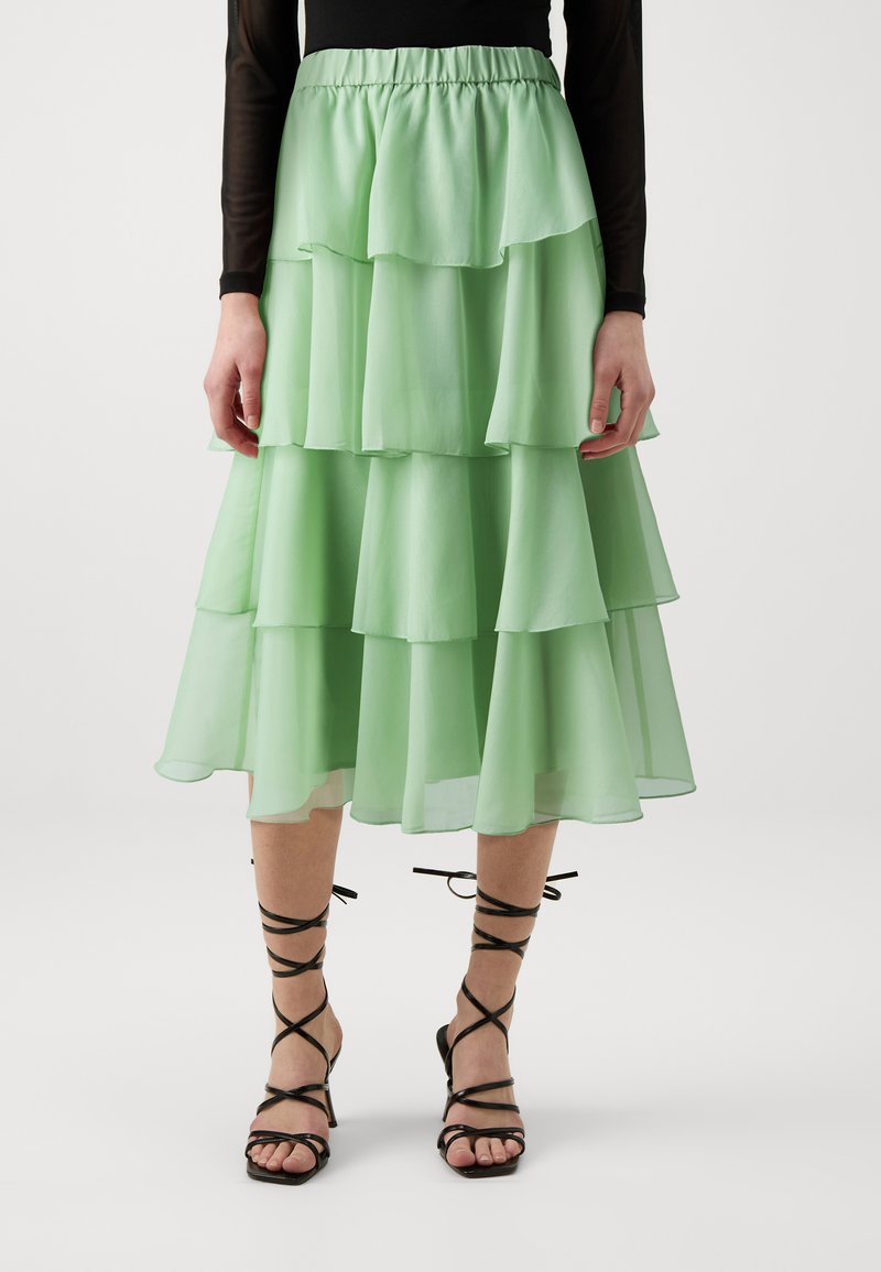 Fustă suprapusă, vaporoasă, de culoare verde mentă, fabricată dintr-un material ușor. Prezintă un tiv elastic și un design stratificat, cu margini franjurate.