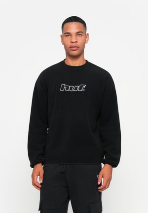 Black sweatshirt made of soft fabric, featuring a crew neckline and a central "huf." logo in white. Worn with black cargo pants.