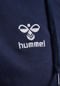 Marineblauwe hoodie met wit geborduurd "hummel" logo en gestileerd bijenontwerp. Heeft een gestructureerde stof en een trekkoordsluiting.