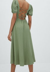 Robe midi verte en tissu texturé et tissé, avec des manches bouffantes et un dos croisé avec des liens. Longueur midi et coupe décontractée.