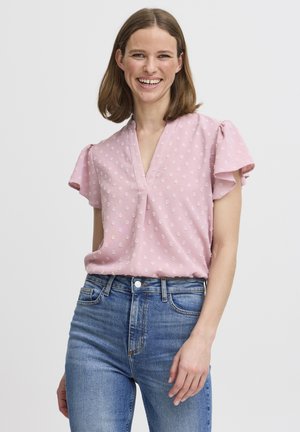 Rosa Bluse mit kurzen fließenden Ärmeln, V-Ausschnitt und strukturiertem Blumenmuster. Kombiniert mit hoch taillierten blauen Jeans.