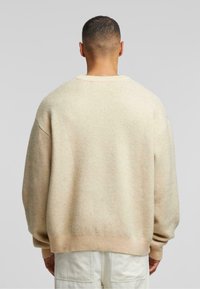 Beżowy sweter z dzianiny o luźnym kroju, z opuszczonymi ramionami, ściągaczami na mankietach i u dołu. Miękka faktura z delikatnymi wariacjami kolorystycznymi.