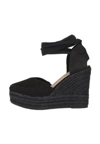 Espadrilles negras con cuña, con una correa de tela en el tobillo, parte superior de ante y suela de yute trenzado, que presentan un diseño texturizado y punta redondeada.