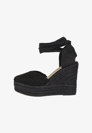 Espadrilles negras con cuña, con una correa de tela en el tobillo, parte superior de ante y suela de yute trenzado, que presentan un diseño texturizado y punta redondeada.