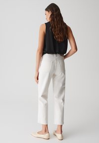 Jeans bianchi a gamba dritta con tasche posteriori, abbinati a un top senza maniche nero. Texture morbida e linee pulite, completati da ballerine color nude.